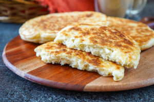 Mkatra Foutra (Sesame Coconut Flatbreads) on a wooden board with one torn in half to show fluffy texture.