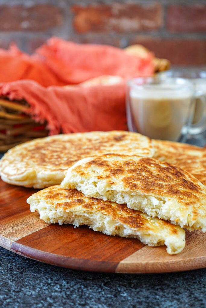 Side view of Mkatra Foutra (Sesame Coconut Flatbreads) on a wooden board with two coffee cups in the background.