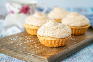 Hertzoggies (South African Jam and Coconut Tartlets) on a wooden board.