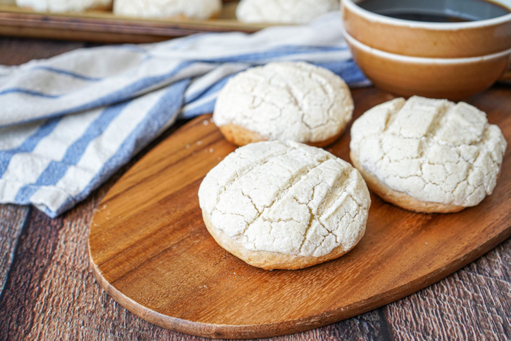 Three Semitas de Yema on a wooden board next to cup of coffee.