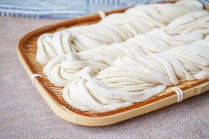 Three bundles of fresh Homemade Udon Noodles on a bamboo plate.
