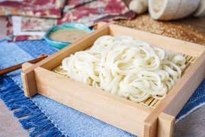 Cold Udon Noodles on a square plate with sesame miso sauce in background.