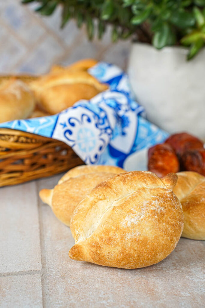 Side view of Papo Secos (Crusty Rolls) with sausages, rolls in a basket, and a green plant in the background.