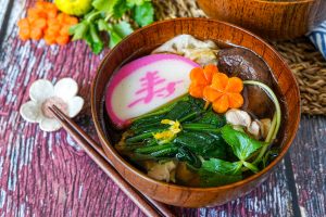 Ozoni (Japanese New Year Mochi Soup) in a wooden bowl with spinach, carrots, mushroom, and fish cake.