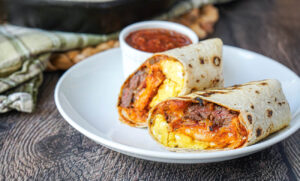 Carne Asado Burritos cut in half and on a white plate with salsa.