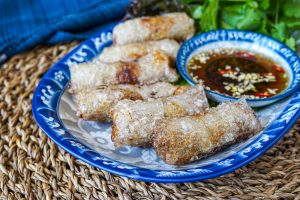 Chả Giò Thịt Heo (Vietnamese Pork Spring Rolls) on a platter with dipping sauce and herbs.