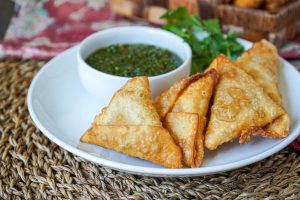 Samosas on a white plate with cilantro and chutney.