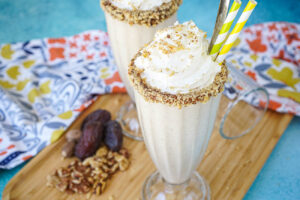 Date Shake in two milkshake glasses next to dates and walnuts.