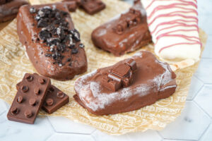 Ice Cream Bars covered in chocolate on a piece of parchment.
