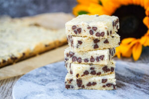A stack of five Chocolate Chip Shortbread Bars with sunflowers in the background.