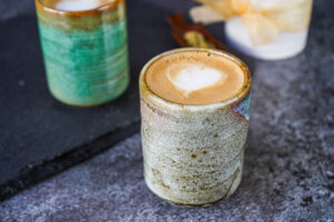 Cardamom Latte in two stone glasses with cardamom pods in the background.
