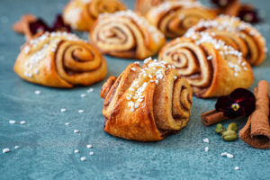 Korvapuustit (Finnish Cinnamon Rolls) next to pansies, cinnamon sticks, and cardamom pods.