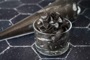 Midnight Black Buttercream in a glass cup with more in a piping bag.