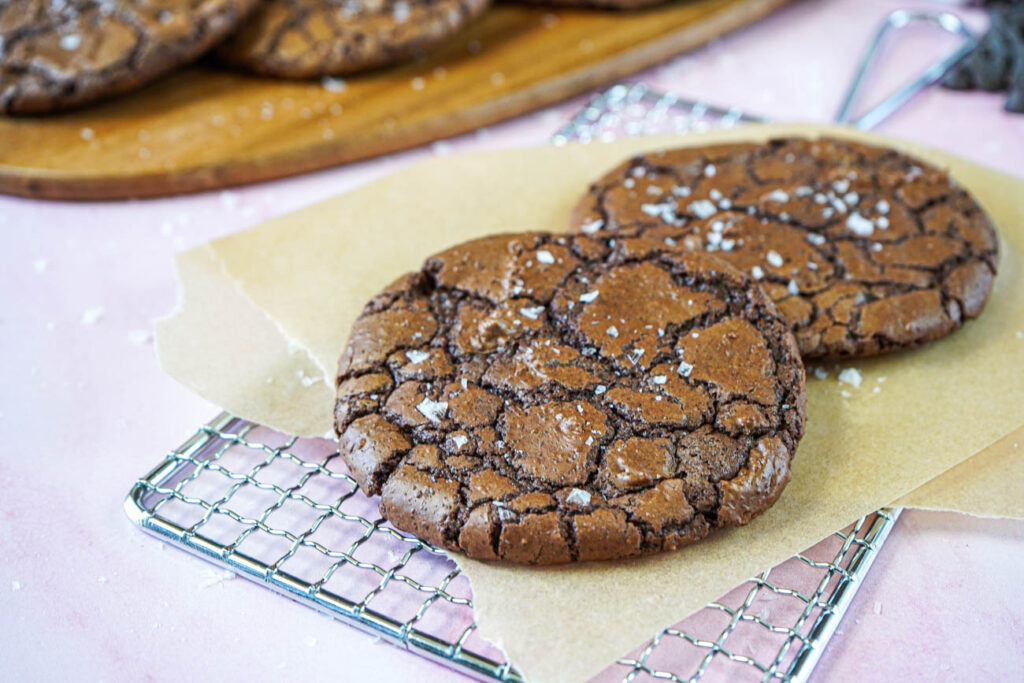 Two Crinkly Brownie Cookies on a parchment lined wire rack.