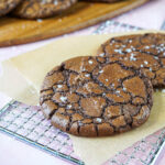 Two Crinkly Brownie Cookies on a parchment lined wire rack.