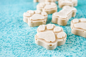Paw and bone shaped Peanut Butter Pupsicles on a blue background.