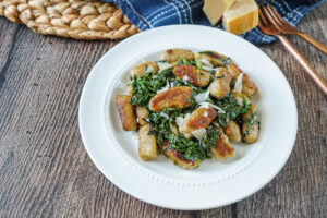Chestnut Gnocchi with Pecorino and Chard on a white plate next to two copper forks.