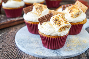 Three S'mores cupcakes on a marble board topped with toasted marshmallows, chocolate, and graham crackers.