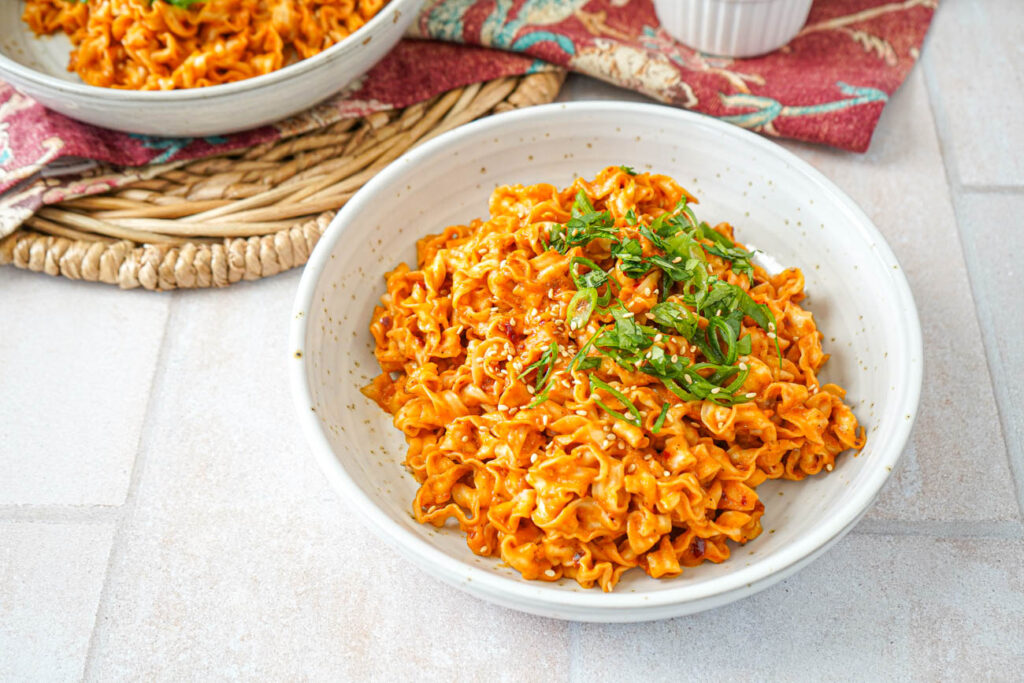 Spicy Peanut Noodles in two bowls with green onions, cilantro, and sesame seeds.