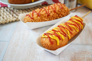 Two Korean Corn Dog in paper holders with ketchup and mustard over the top.