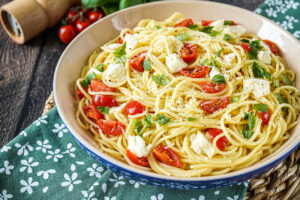Spaghetti alla Caprese (Spaghetti from Capri) in a large bowl with pepper grinder, cherry tomatoes, and basil in background.