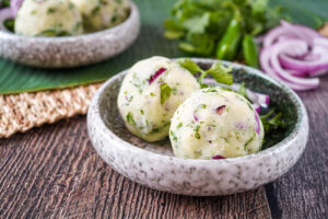 Aloo Shedo (Bengali Mashed Potato) in two balls on a plate with cilantro and red onion.