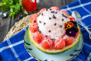 Watermelon Shave Ice in a watermelon bowl with fresh watermelon balls, chocolate chips, and pansies.