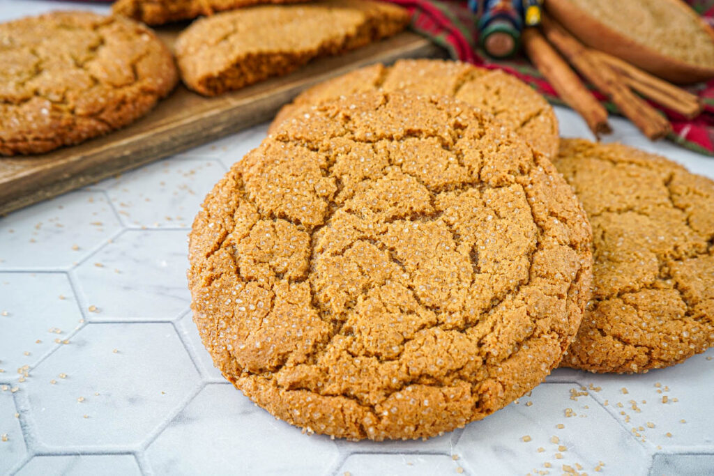Close up of three Giant Gingersnap Cookies with more in the background next to cinnamon sticks.