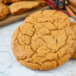 Close up of three Giant Gingersnap Cookies with more in the background, cinnamon sticks, and turbinado sugar.