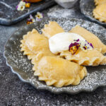 Five Pierogi with Sweet Cream Cheese on a gray plate with sour cream and pansies.