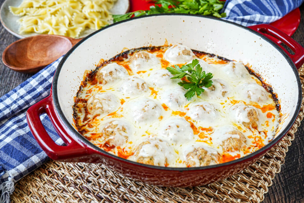 Effortless Chicken Meatball Marinara in a red pan covered in melted cheese.