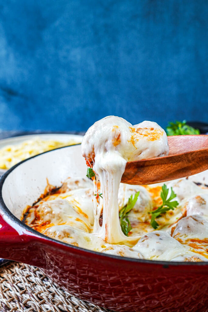 Wooden spoon lifting two meatballs and cheese from the pan.
