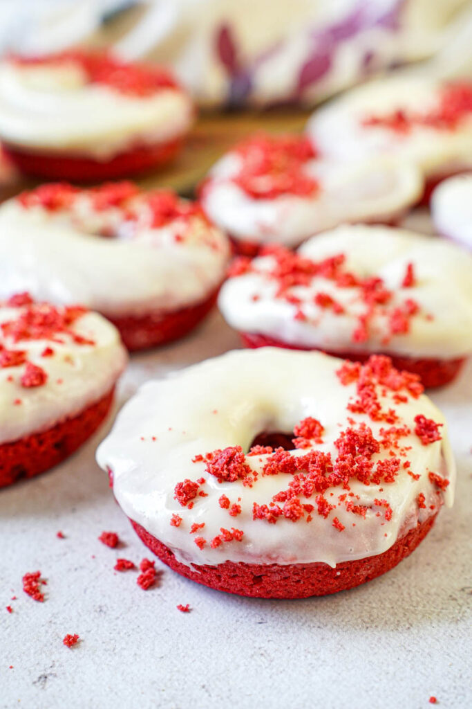 Side view of Baked Red Velvet Donuts topped with a cream cheese glaze and red velvet crumbs.