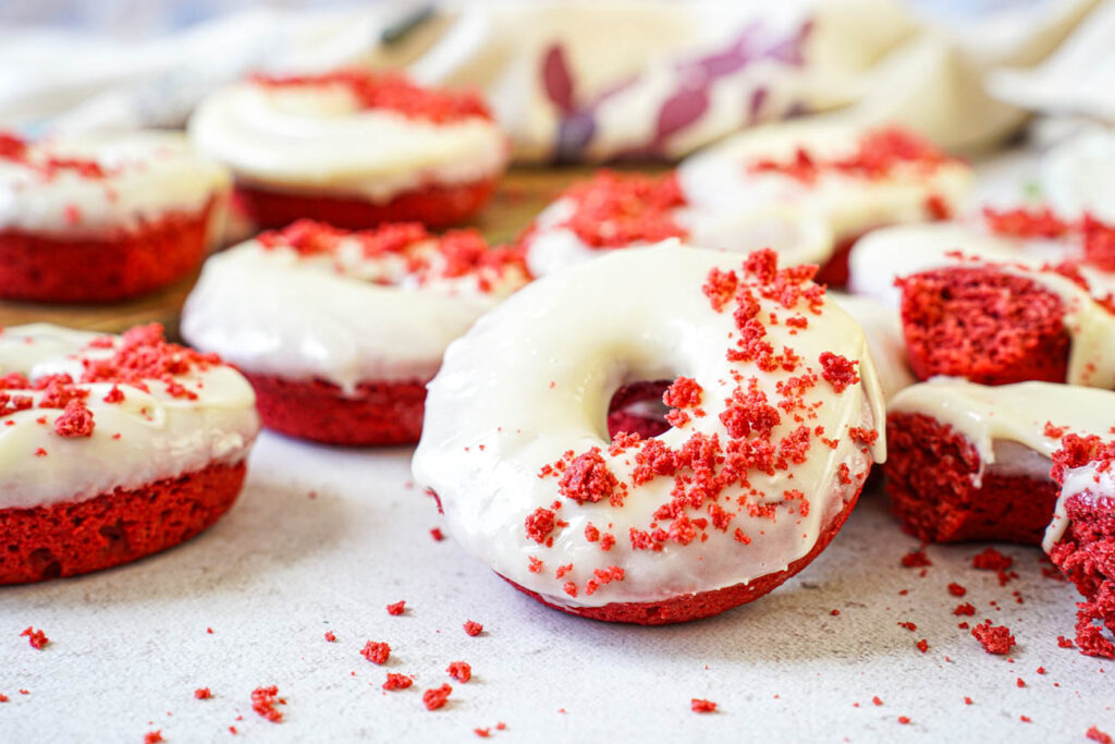 Baked Red Velvet Donuts topped with a cream cheese glaze and surrounded by red velvet crumbs.
