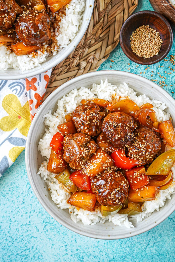 Aerial view of Sweet and Sour Pineapple Meatballs and rice in two bowls next to a bowl of sesame seeds.