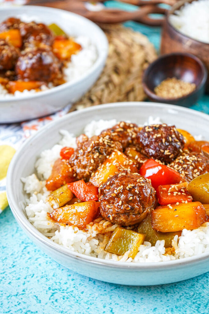 Close up of Sweet and Sour Pineapple Meatballs in a bowl with sesame seeds, rice, and another bowl in the background.