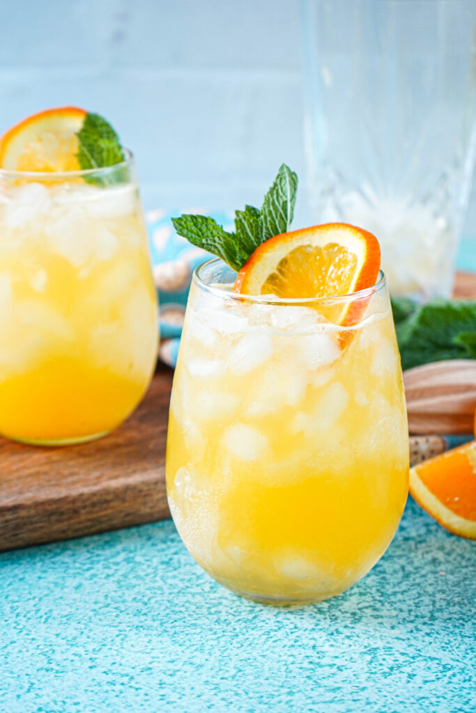 Side view of Creamsicle Crush in two glasses with orange slices and mint sprigs.