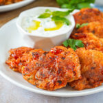 Santorini Tomato Patties (Tomatokeftedes Santorinis) on a white plate next to a bowl of tzatziki.