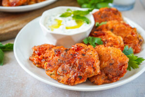 Santorini Tomato Patties (Tomatokeftedes Santorinis) on a white plate next to a bowl of tzatziki.