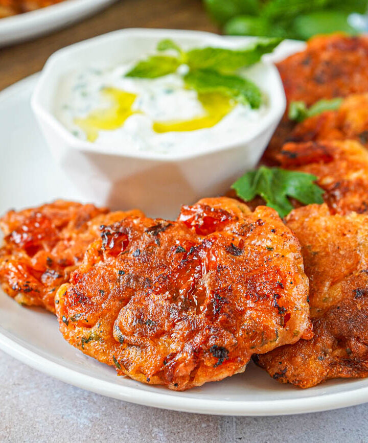 Santorini Tomato Patties (Tomatokeftedes Santorinis) on a white plate next to a bowl of tzatziki.
