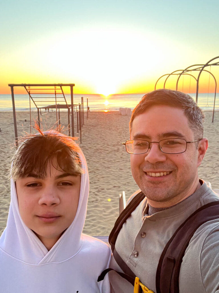 Dad and son standing in front of beach sunrise.