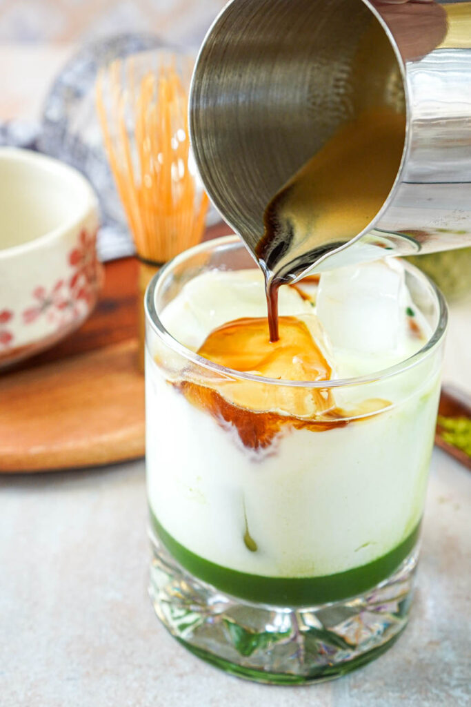 Pouring espresso into a glass of milk and matcha over ice.