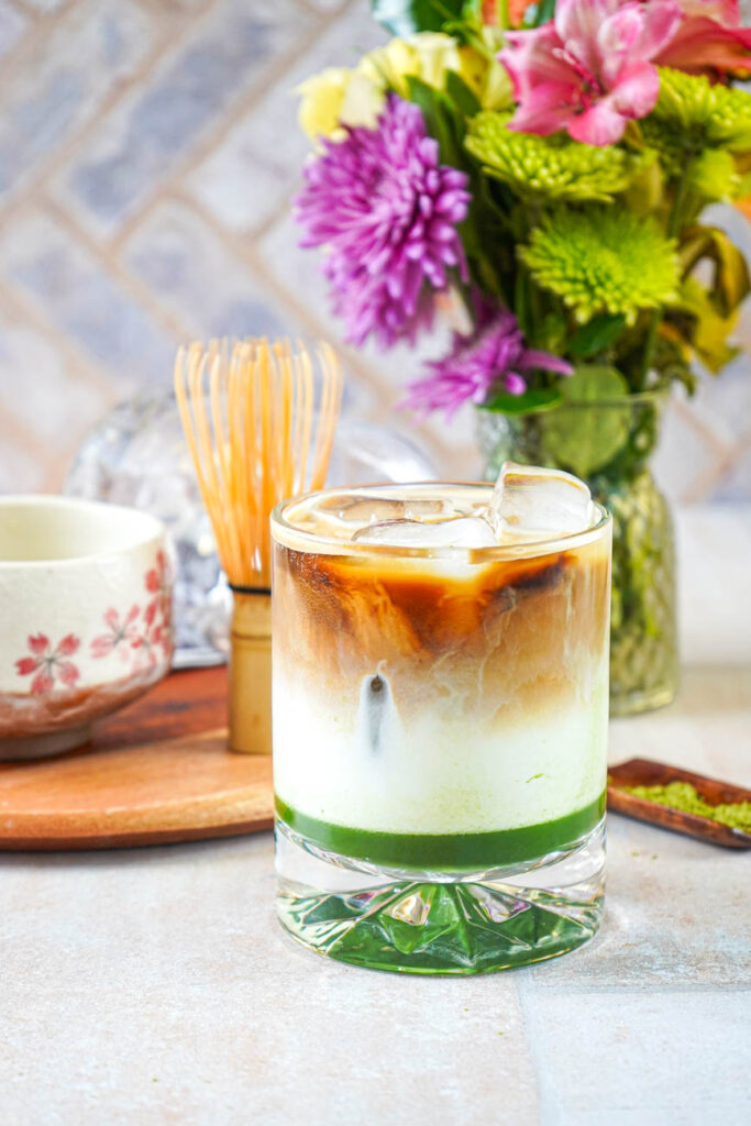 Close up of Iced Matcha Espresso Latte in a glass with layers of matcha, milk, and espresso on top.