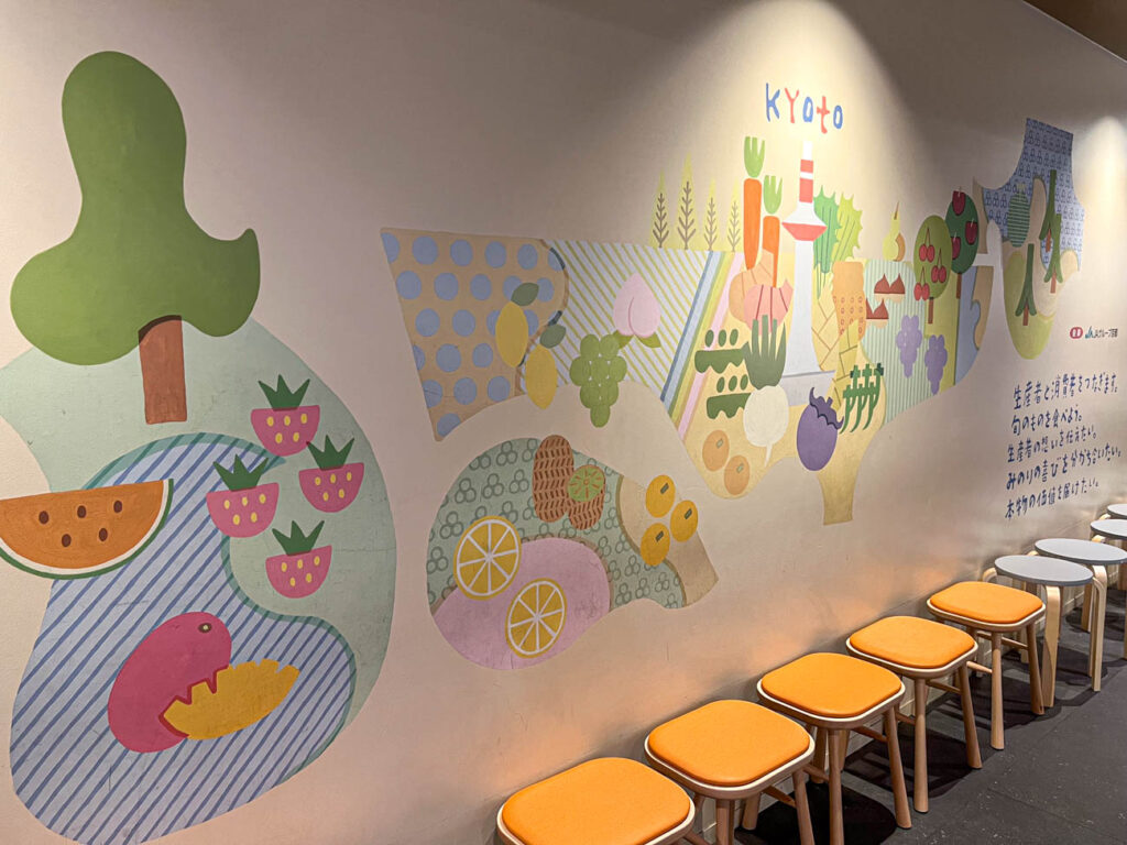 Colorful mural of Kyoto with fruits and vegetables on a wall lined with stools.