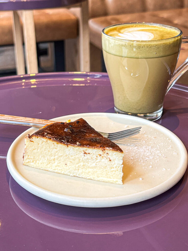 Basque Cheesecake on a plate next to an Espresso Matcha Latte.