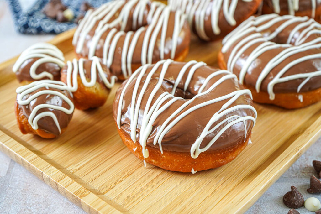 Milk Chocolate Donuts with a white chocolate drizzle on a wooden baking sheet.