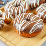 Milk Chocolate Donuts and donut holes with a white chocolate drizzle on a wooden tray.
