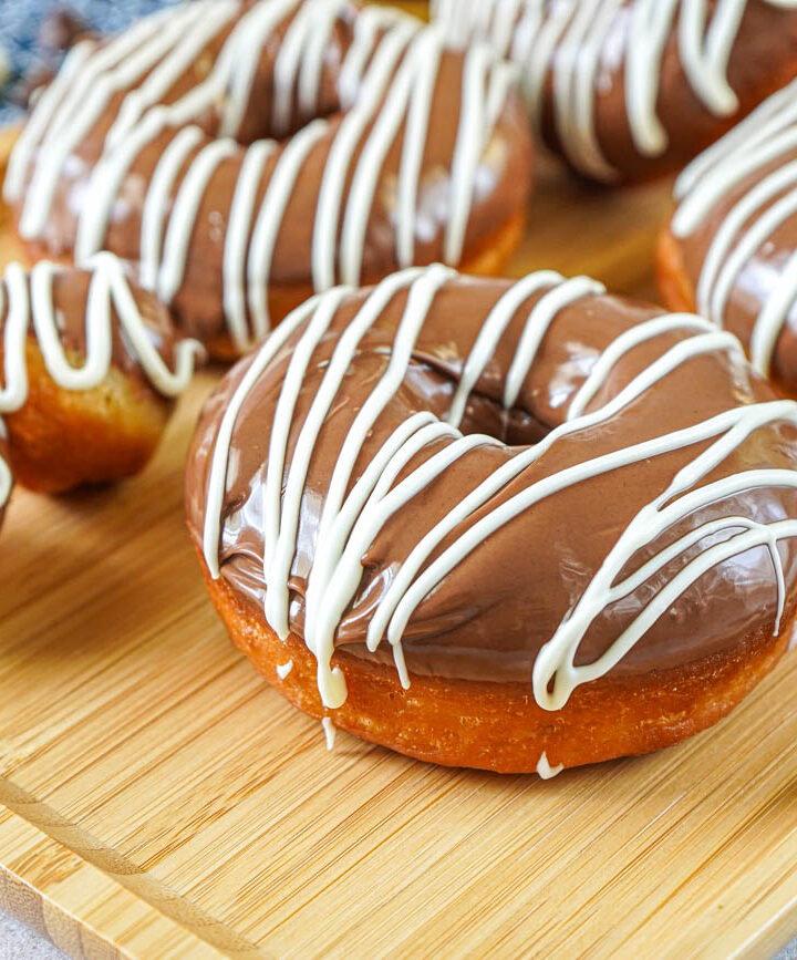 Milk Chocolate Donuts and donut holes with a white chocolate drizzle on a wooden tray.