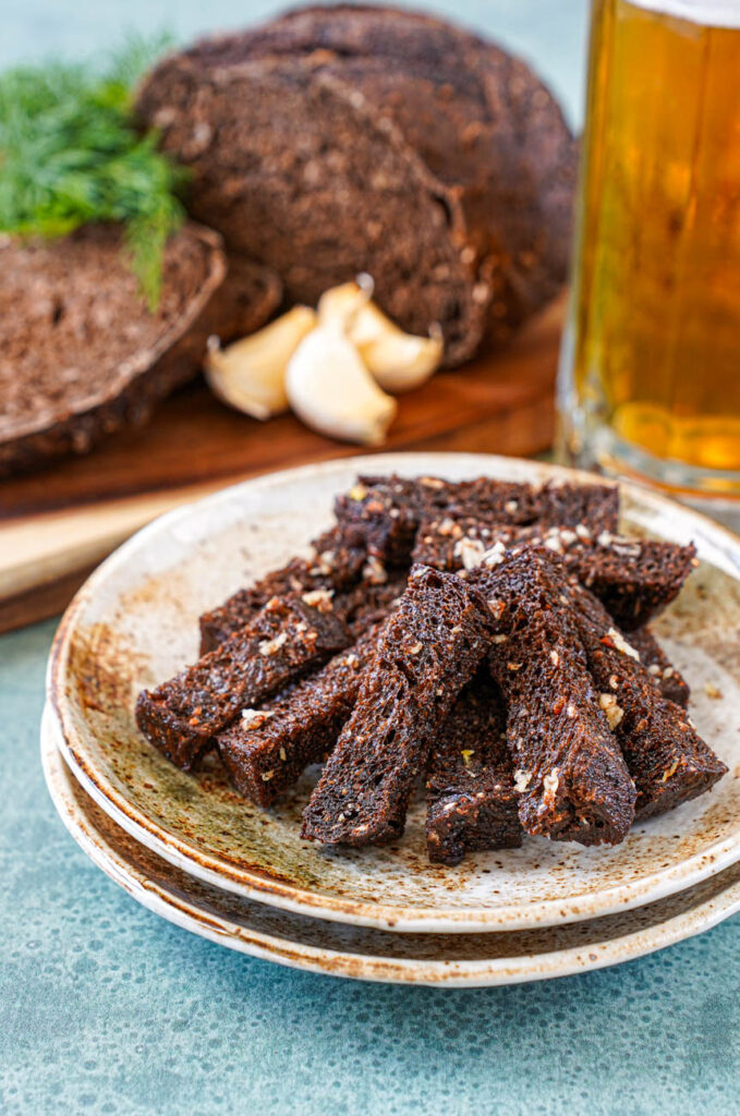 Close up of Baltic Fried Bread on a plate with beer, garlic cloves, and black bread in the background.