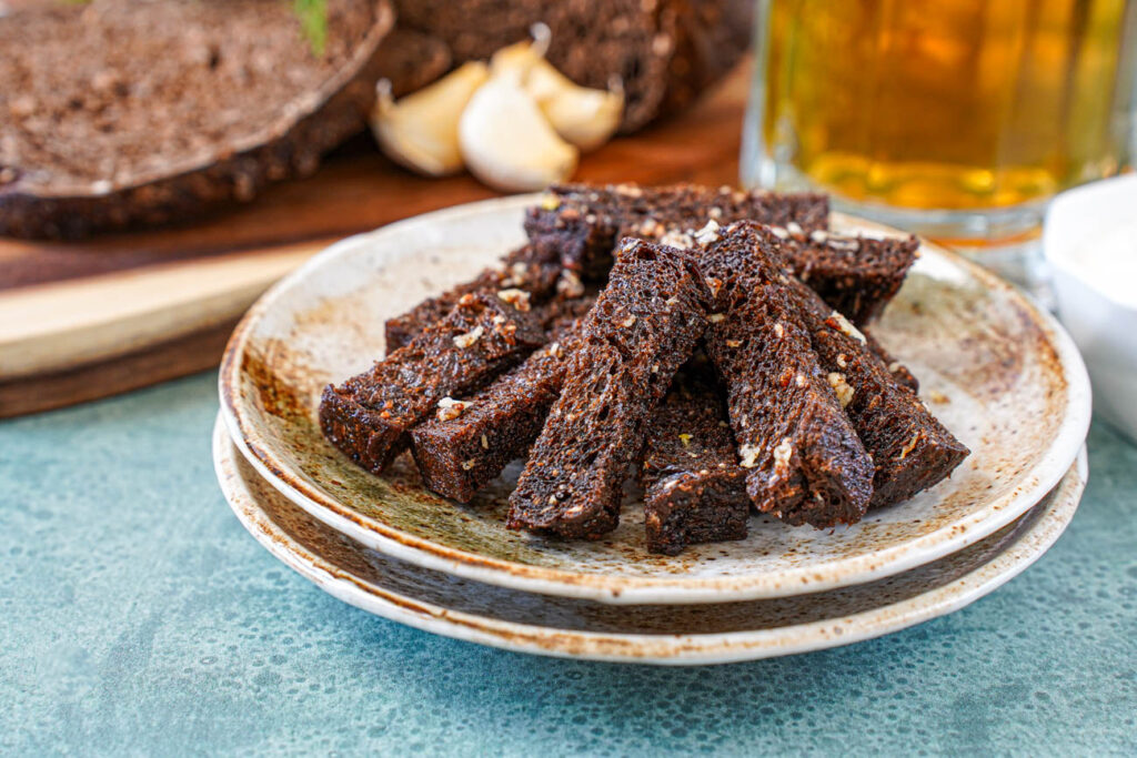 A pile of Baltic Fried Bread on two brown plates with a mug of beer and garlic cloves in the background.